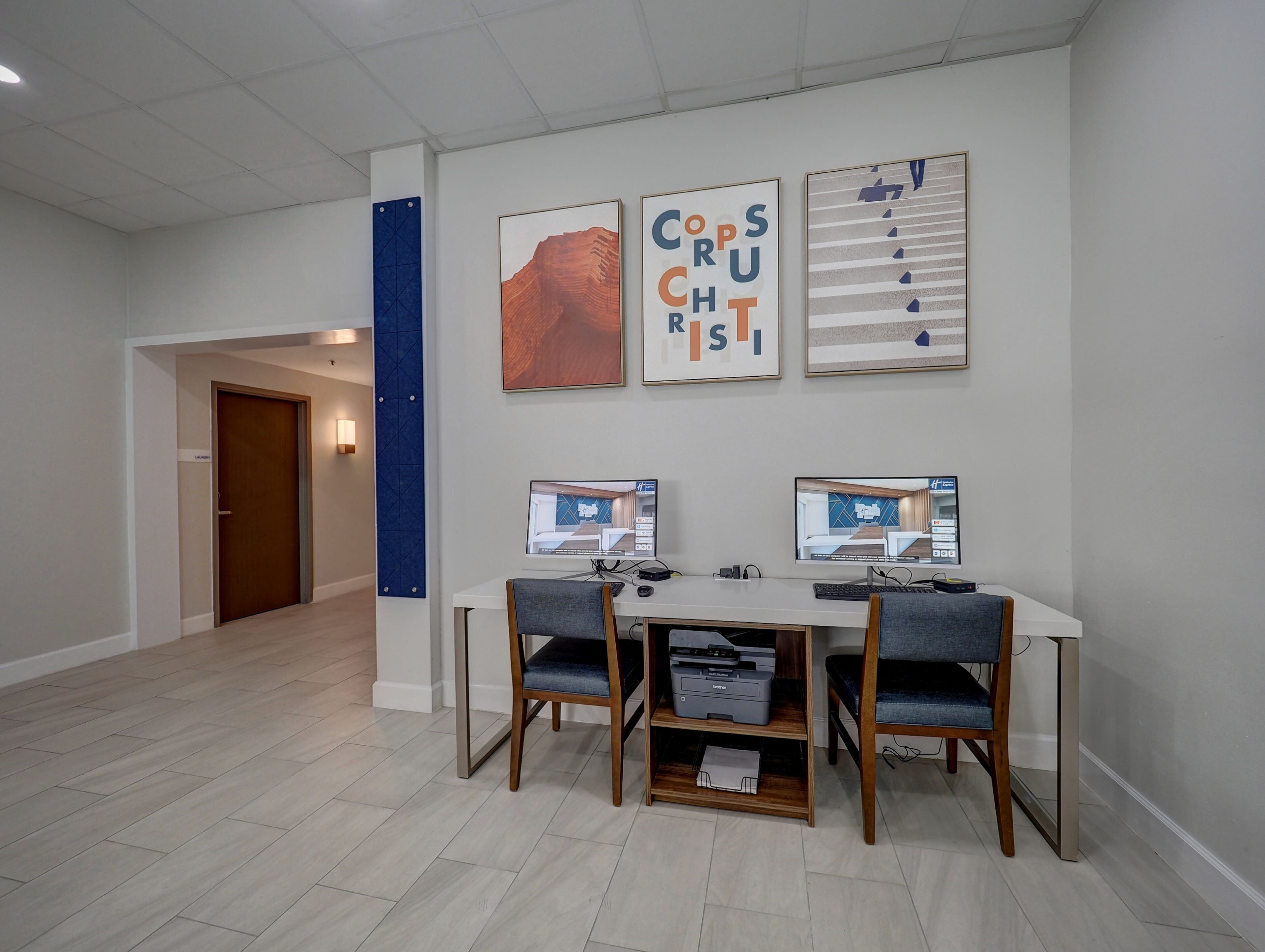 Un espacio de oficina moderno con un escritorio blanco, dos monitores e impresora. Hay tres obras de arte enmarcadas en la pared y una pared de acento azul.