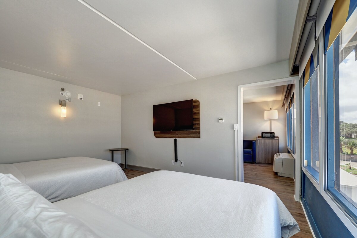 Une chambre d’hôtel avec deux lits, un téléviseur fixé au mur, une petite table et une vue sur l’extérieur par une fenêtre.