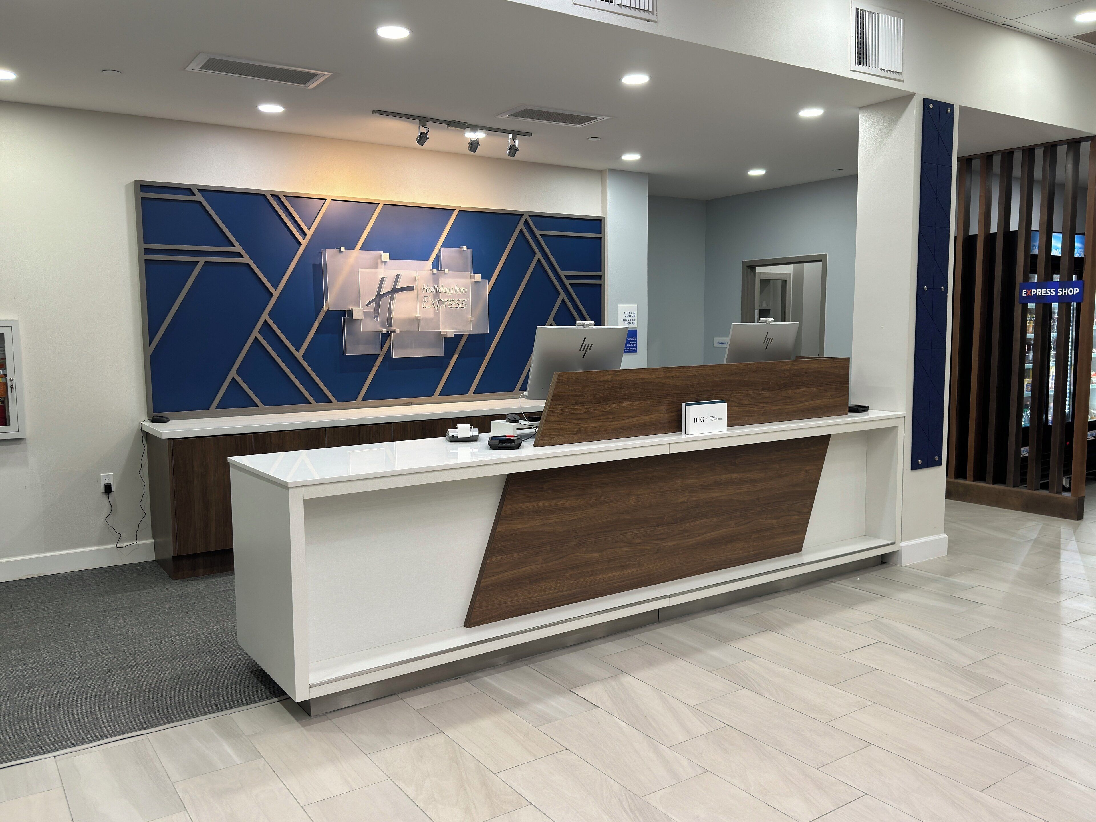 A hotel reception desk with a modern design, a digital screen, and a sign indicating an express shop.