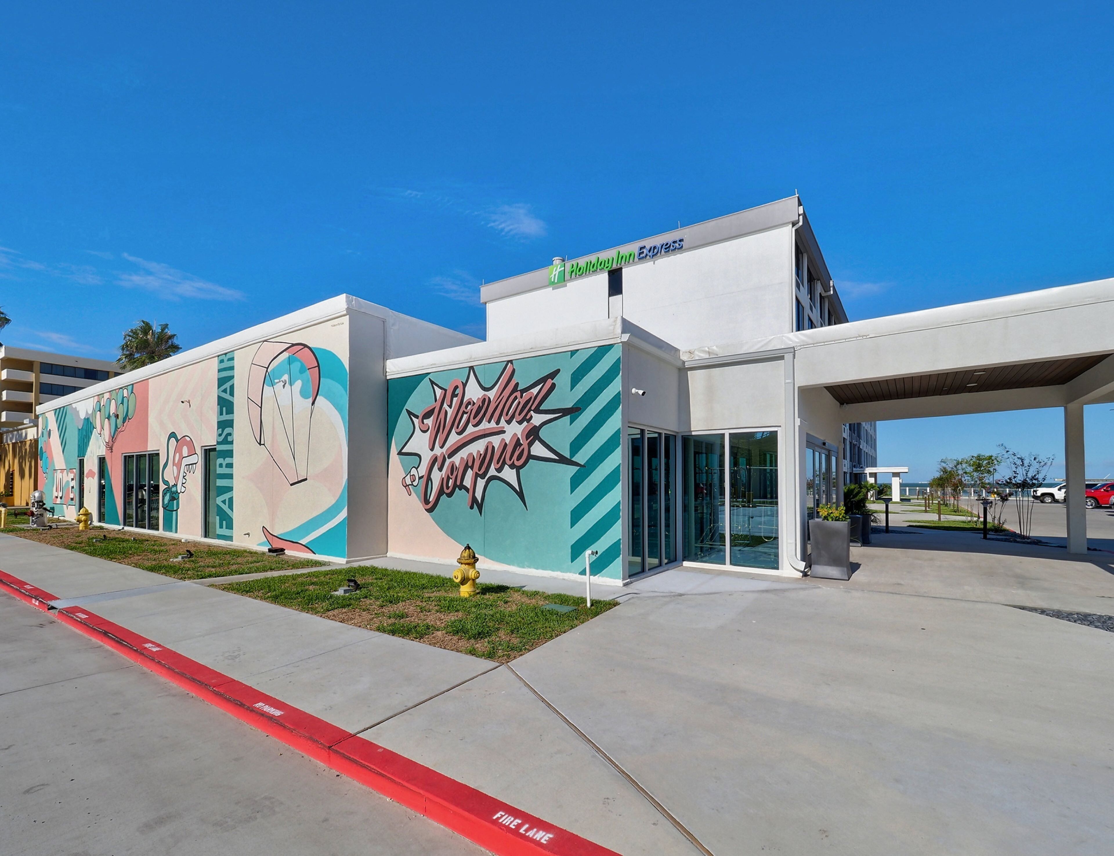 A modern building with a colorful mural, a Holiday Inn Express sign, and a fire lane.