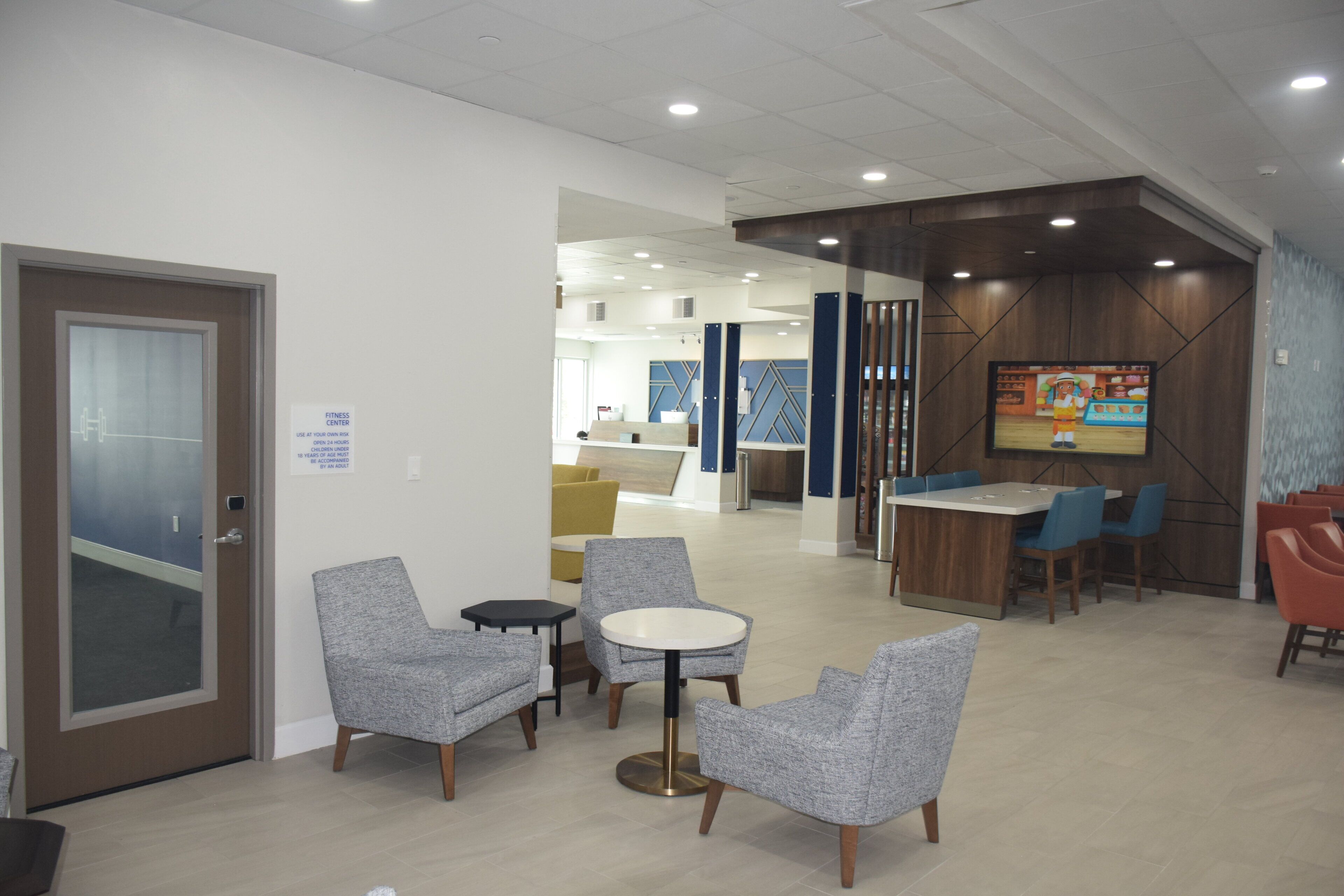 A modern lobby with seating areas, a reception desk, and a fitness center sign.