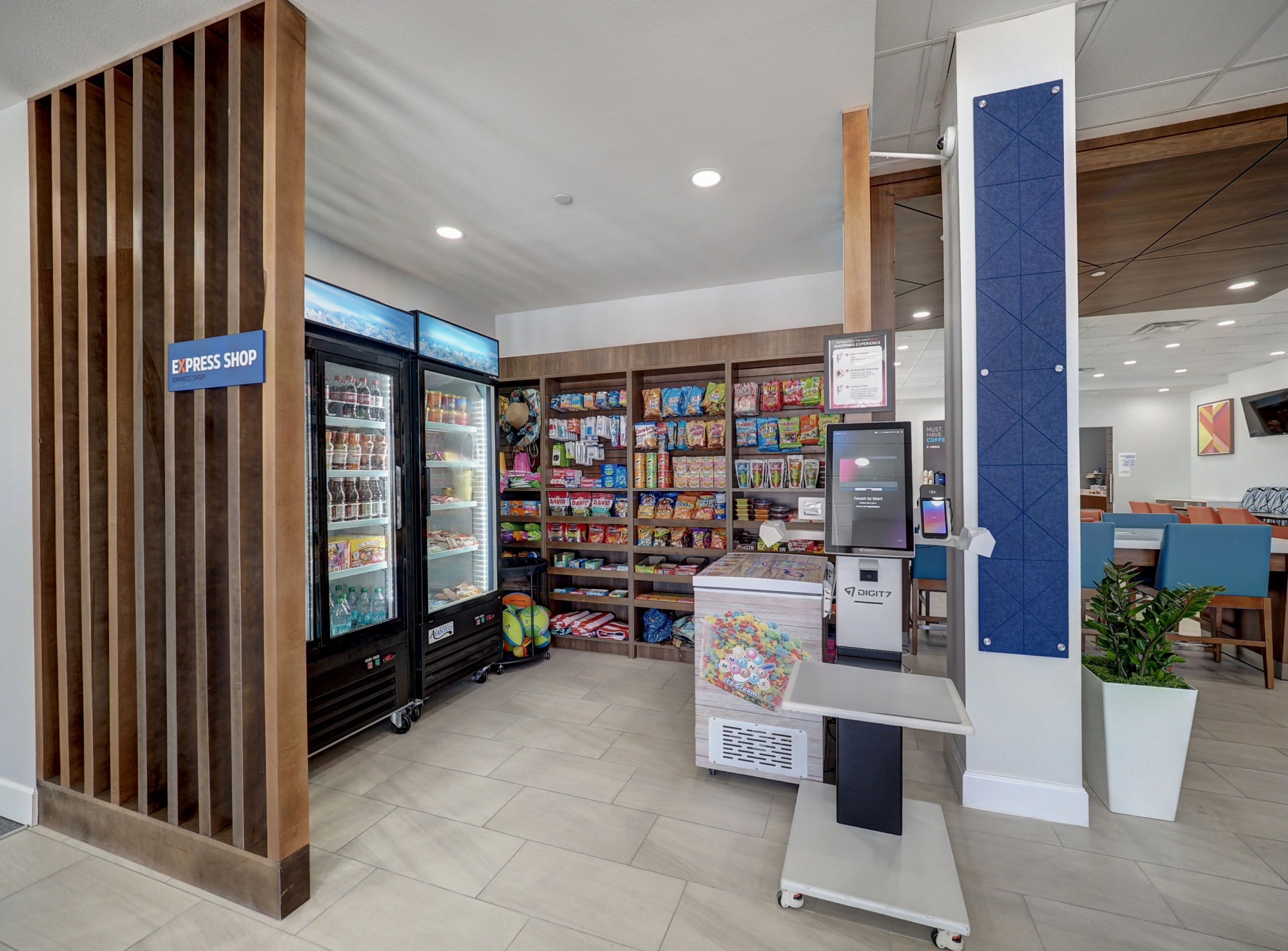 A self-service kiosk area with a refrigerated display, shelves stocked with snacks, and a coffee machine.