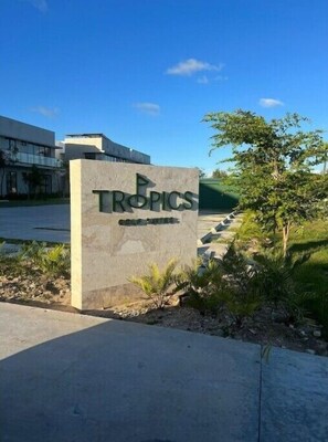 A sign for Tropics with a modern building in the background. - Jimbo's Place. (Punta Cana)