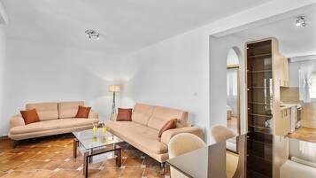 A modern living room with a beige sofa, a glass coffee table, and a dining area with a wooden table and chairs.