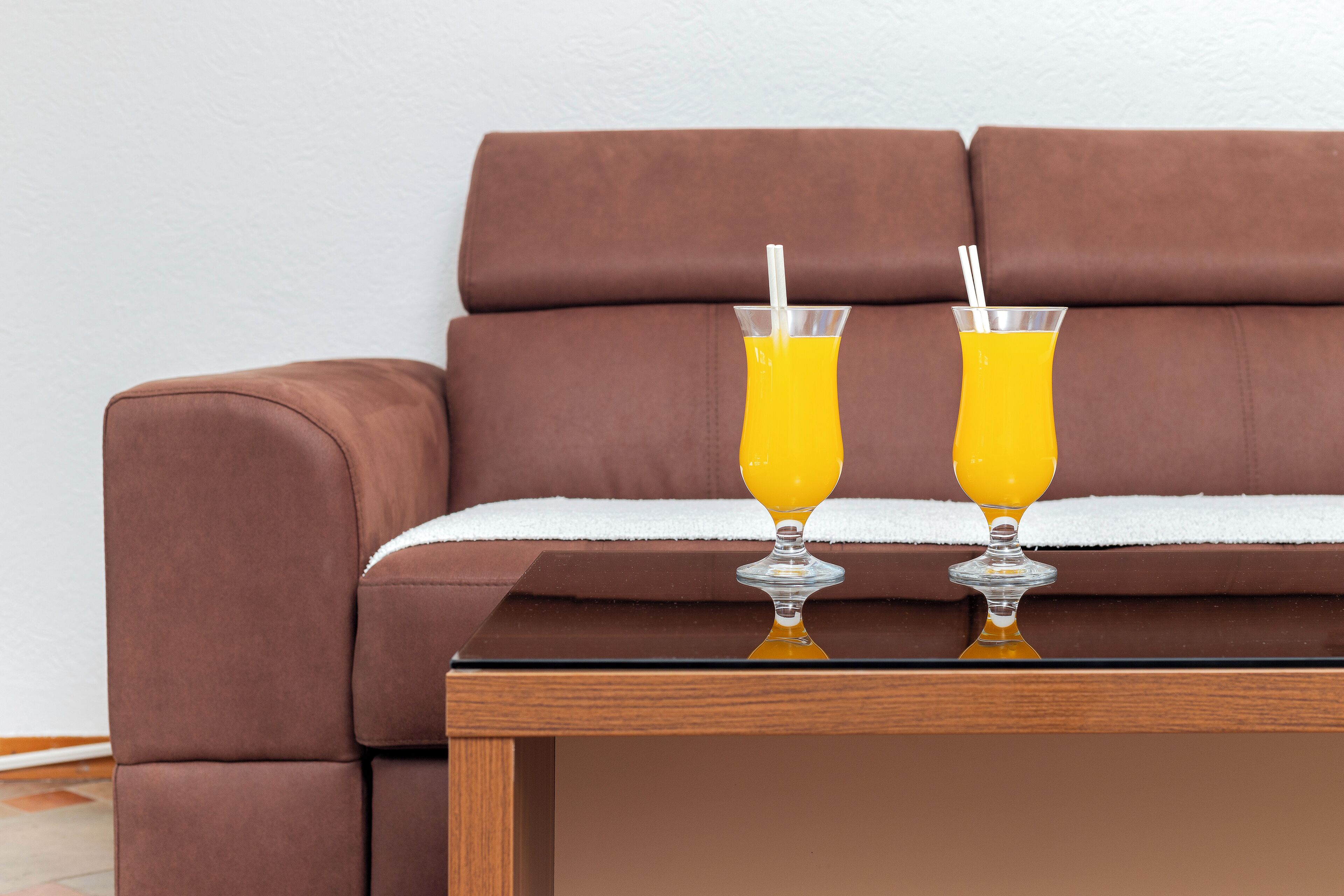 A brown leather sofa with a white throw blanket and two glasses of orange juice on a wooden table.