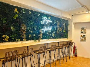 A bar area with a neon sign reading "Boga Hotel" and a wall decorated with various plants. - Boga Hostel (Madrid)
