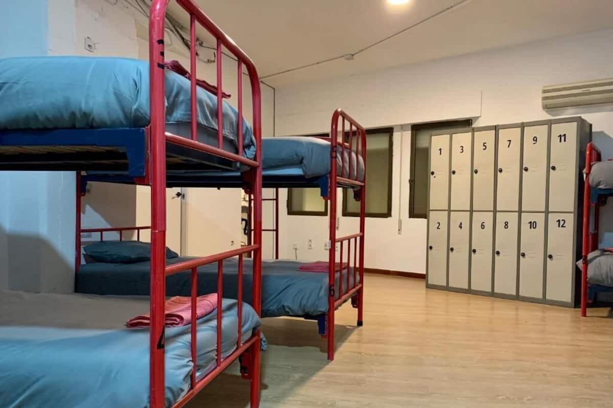 A dormitory room with bunk beds, a wardrobe with numbered lockers, and a wooden floor.