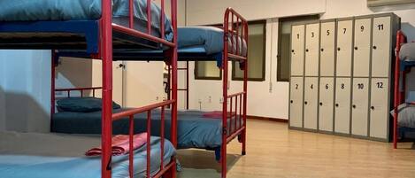 A dormitory room with bunk beds, a wardrobe with numbered lockers, and a wooden floor.
