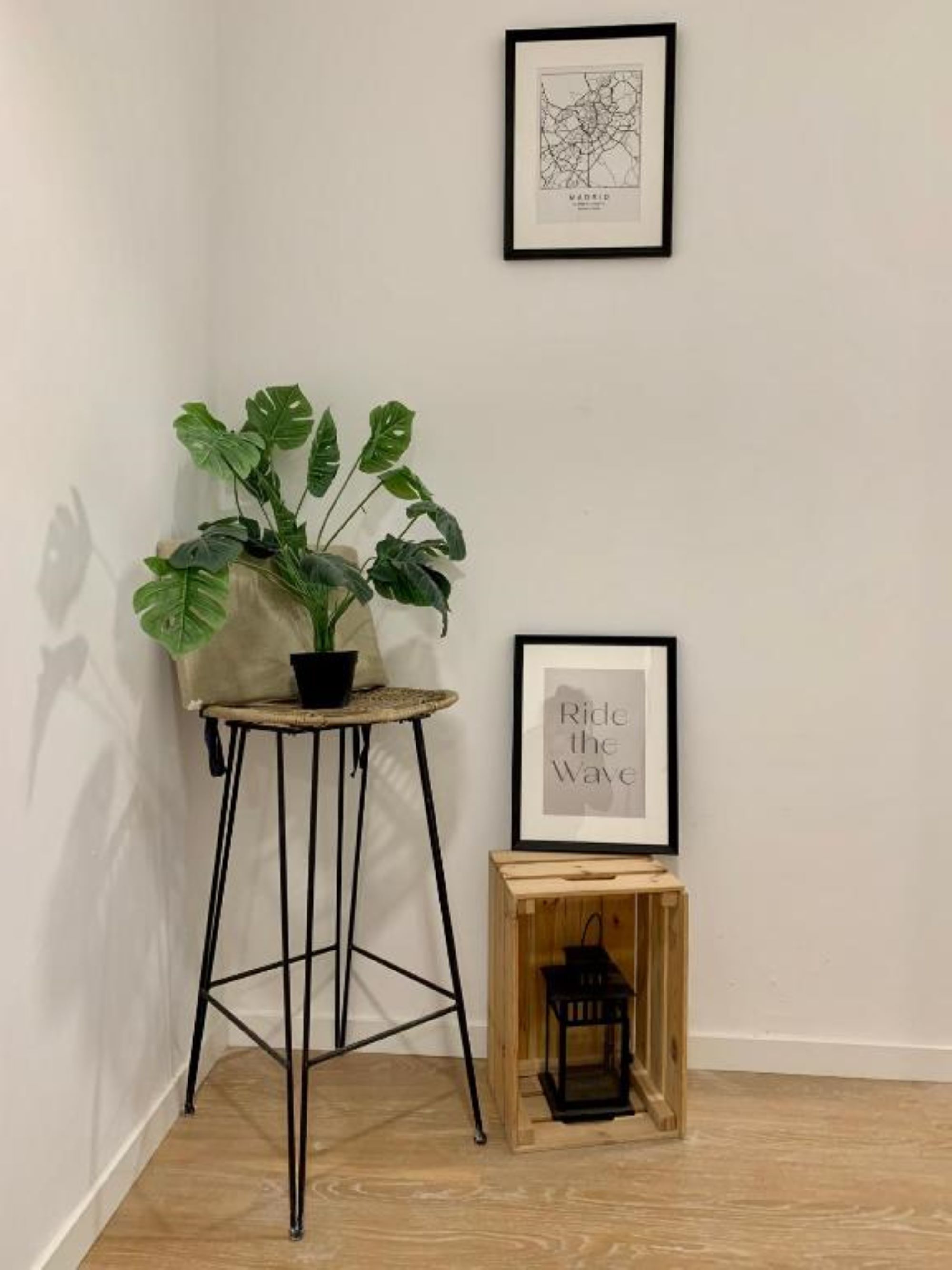 A corner room with a potted plant on a stool, a framed map, and a framed quote on the wall.