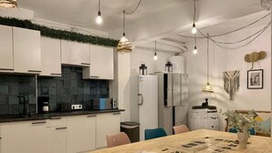 A modern kitchen with white cabinets, a black tiled backsplash, and a wooden dining table with chairs. - Boga Hostel (Madrid)