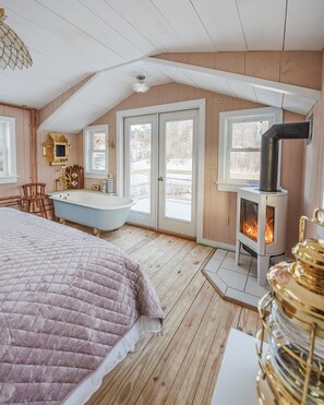 Een gezellige slaapkamer met een groot bed, een houten vloer, een wit plafond en een open haard.