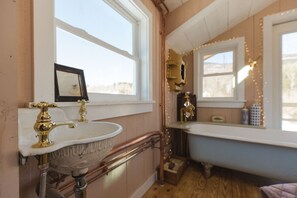 Een badkamer met een oudhollandse wastafel, een badkuip en een raam met lichtslingers.