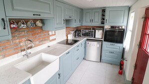 Una cocina con armarios azul claro, pared de ladrillo, un fregadero, microondas, horno y extintor.