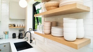 Une cuisine moderne avec des carreaux blancs, des étagères en bois et un évier noir.