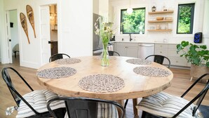 Un coin repas avec une table ronde en bois, six chaises et un vase de fleurs.