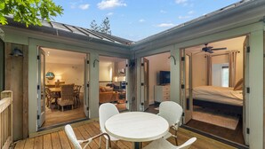 A cozy patio area with a round table and chairs, a wooden deck, and a view into the interior of a house with a dining area, a living room, and a bedroom. - Charming Serenbe Carriage House (Palmetto)