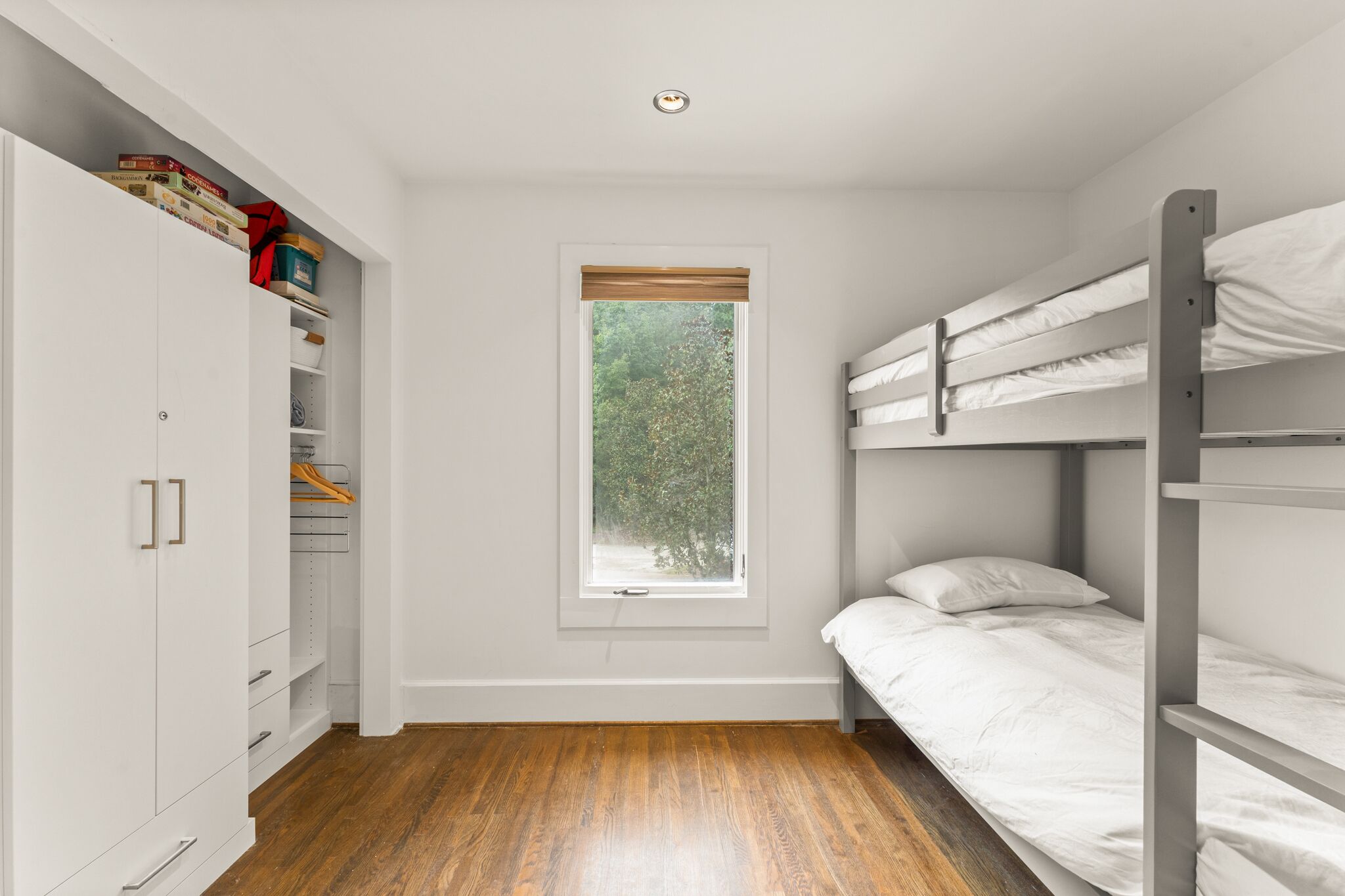 Un dormitorio con una cama litera, un armario, una ventana con vistas a árboles y una lámpara en el techo.