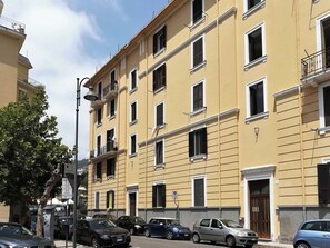Un immeuble jaune à plusieurs étages, doté de balcons, avec des voitures garées et un lampadaire.