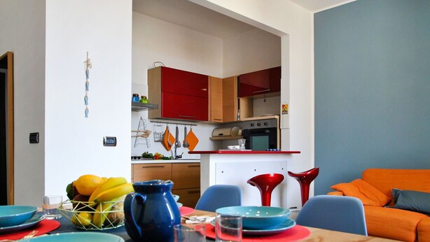 A modern kitchen with red cabinets, a white countertop, and a dining area with a table set for two. - Lovely apartment for 4 people with A/C, WIFI, balcony and pets allowed (Formia)