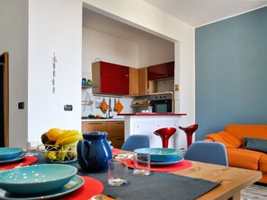 A modern kitchen with red cabinets, a white countertop, and a dining area with a table set for two. - Lovely apartment for 4 people with A/C, WIFI, balcony and pets allowed (Formia)