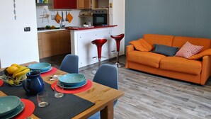 A modern kitchen with red cabinets, a dining area with a wooden table, and an orange sofa. - Lovely apartment for 4 people with A/C, WIFI, balcony and pets allowed (Formia)