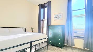 A bedroom with a bed, a dresser, a window with curtains, and a wall-mounted sign.