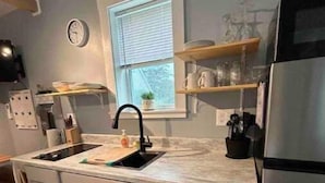 A kitchen with a sink, stove, and refrigerator. There is a window with blinds, a clock on the wall, and shelves with dishes. - Simplicity-Just what you need! STR24-20 (Rockland)