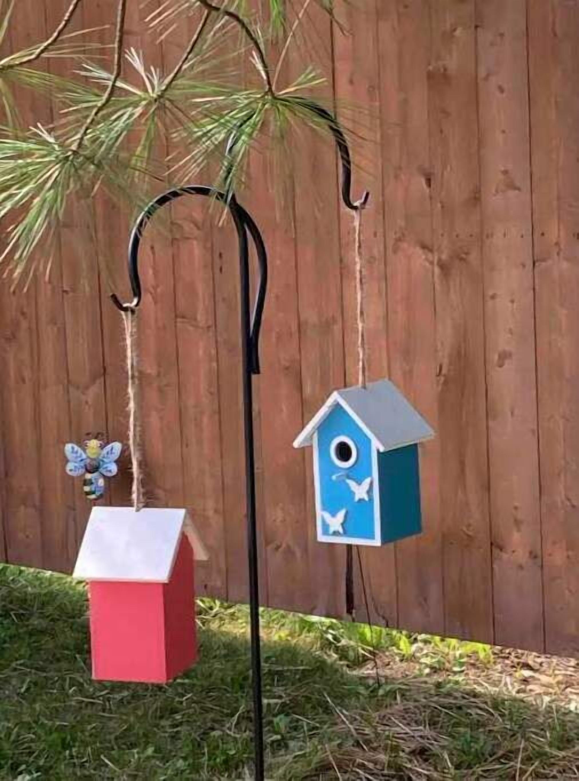 A birdhouse and feeder hanging from a metal hook against a wooden fence.