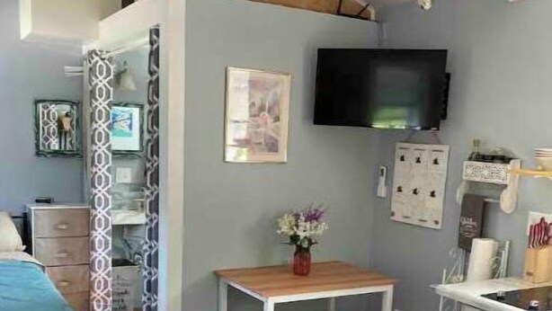 A compact bedroom with a bed, a small table, a bench, a TV, and a kitchenette. - Simplicity-Just what you need! STR24-20 (Rockland)