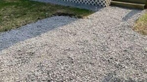 A small, single-story mobile home with a front porch and a gravel driveway. - Simplicity-Just what you need! STR24-20 (Rockland)