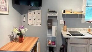 A compact kitchen with a wooden table, a built-in shelf, a clock, and a TV mounted on the wall. - Simplicity-Just what you need! STR24-20 (Rockland)