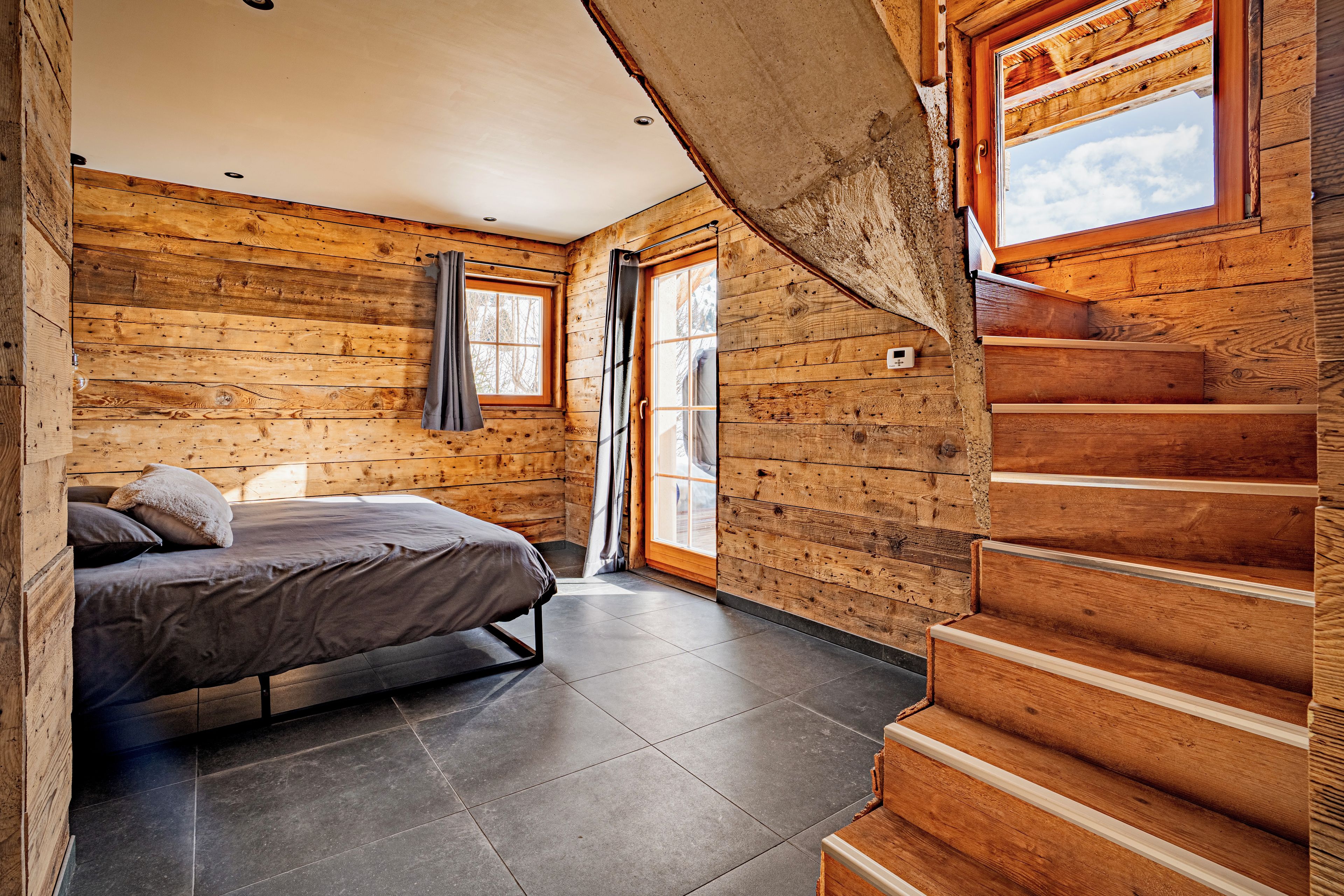 Une chambre aménagée dans un chalet en rondins, avec un lit, une fenêtre et un escalier.