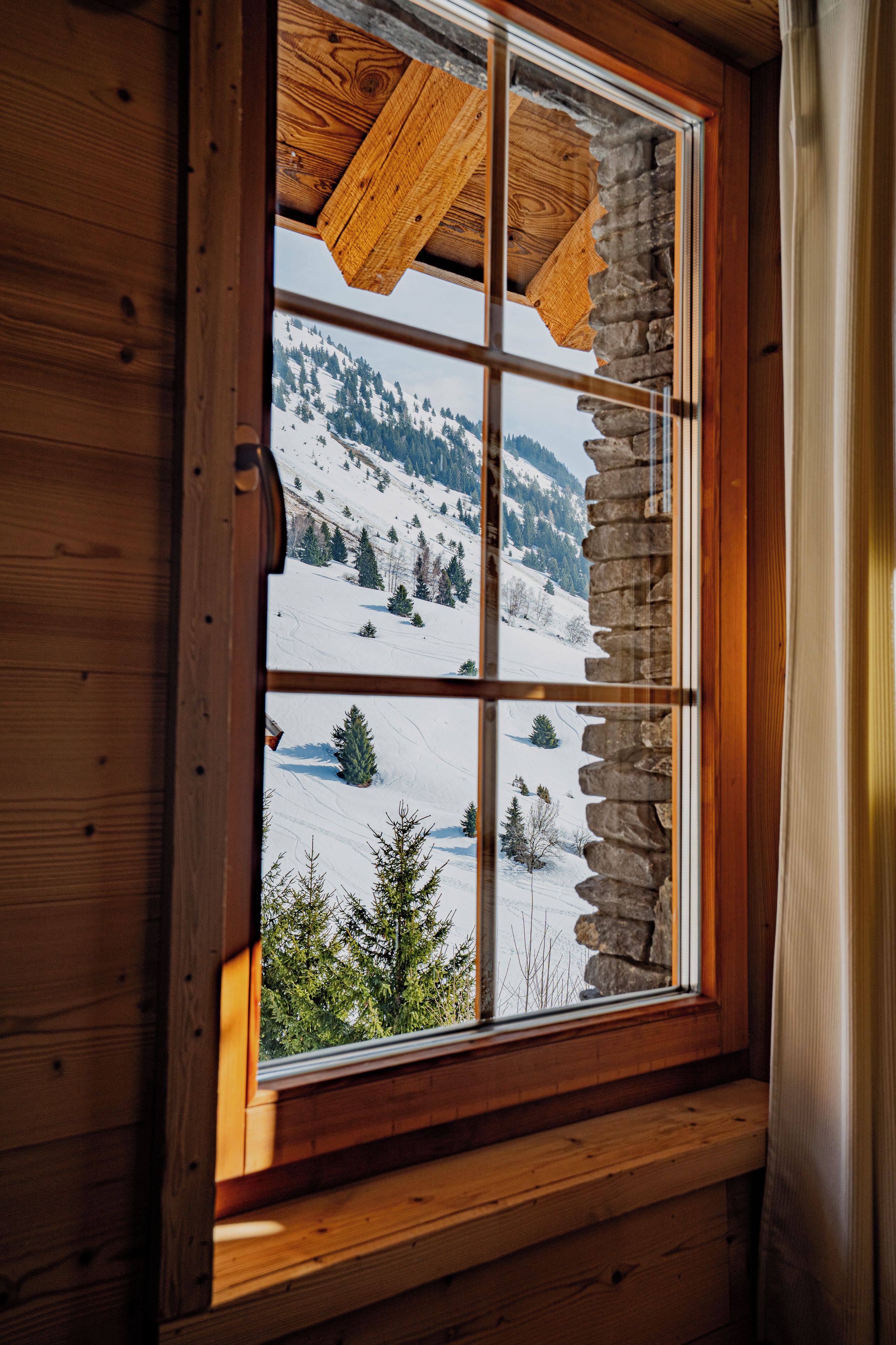 A window with a stone frame and wooden beams, offering a view of a snowy mountain landscape.