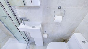A modern bathroom with a glass shower enclosure, a white sink, and a toilet. - Carlton Residence Sleeps 6 (London)