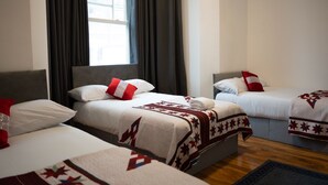 A hotel room with three beds, each with a quilted blanket and pillows. - Carlton Residence Sleeps 6 (London)