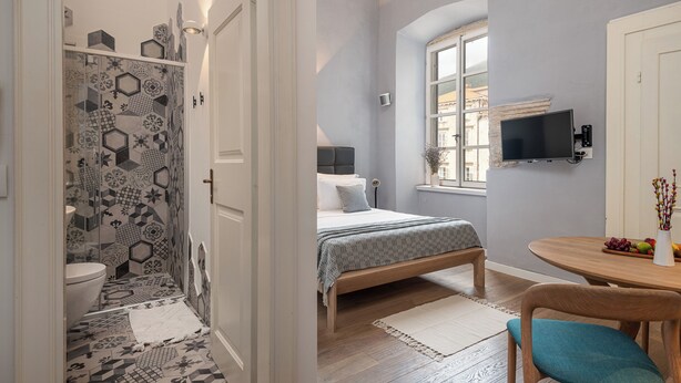 Un dormitorio con cama, mesita de noche, televisor y ventana.