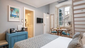 Habitación de hotel con cama, escritorio y silla, una mesita con otra silla, televisor montado en la pared y un cuadro enmarcado.