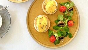 Una mesa de desayuno con platos de comida, un vaso de jugo de naranja y una bolsita de té.