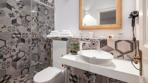 Un baño con lavamanos blanco, un espejo y una ducha con azulejos estampados.
