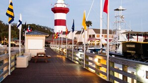 Un paseo marítimo con un faro, una pasarela de madera y una hilera de banderas.