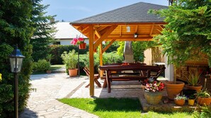 A covered outdoor seating area with a stone pathway leading to it, surrounded by potted plants and a well-maintained garden.