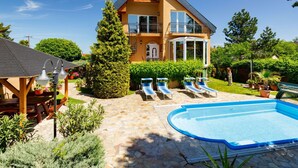 A two-story house with a swimming pool, a covered patio, and a well-maintained garden.
