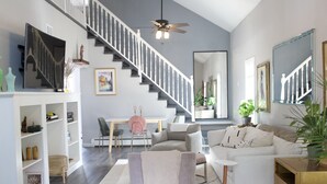 Una sala de estar moderna con una escalera, un televisor de pantalla plana, un comedor y un espejo grande.