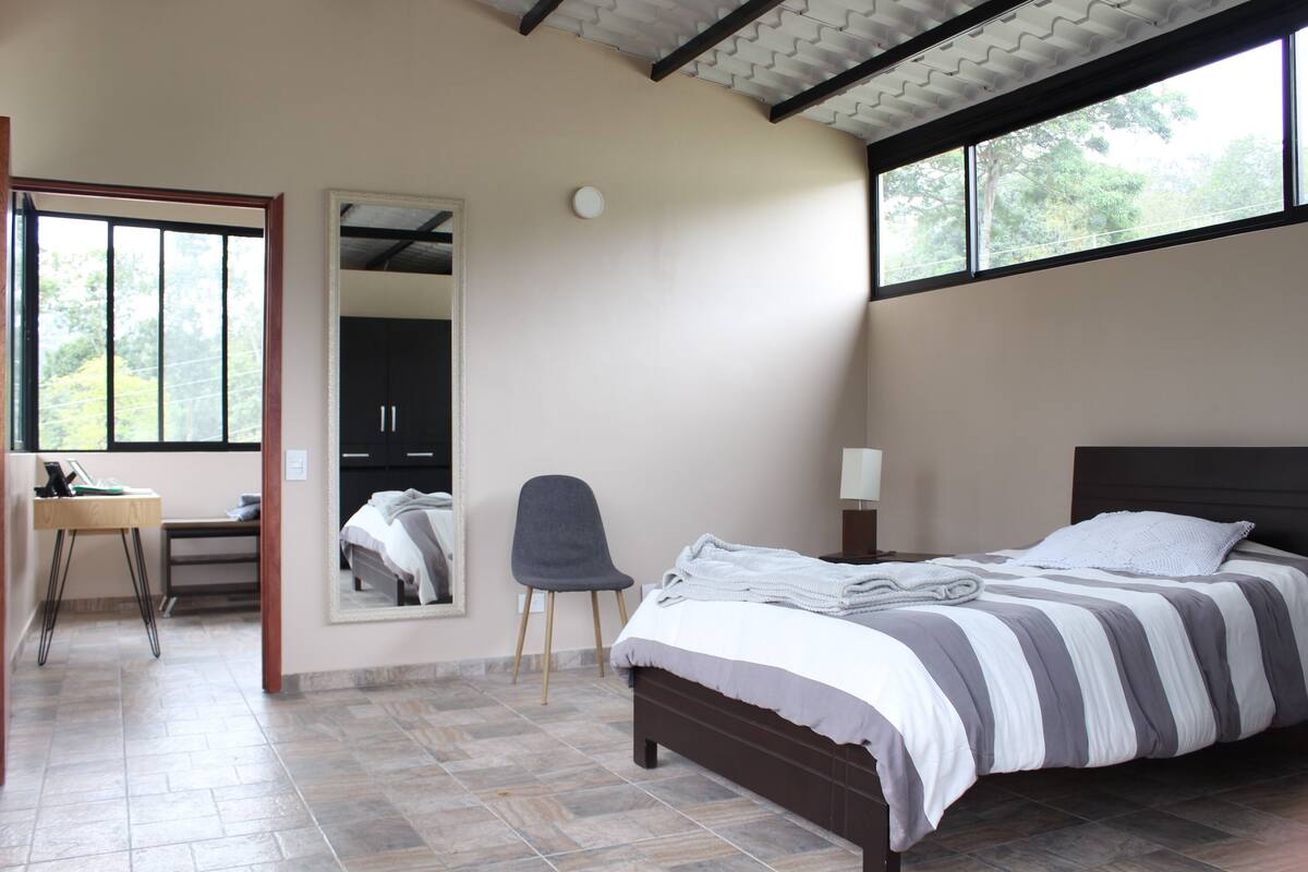 Un dormitorio con cama, silla, escritorio y espejo.