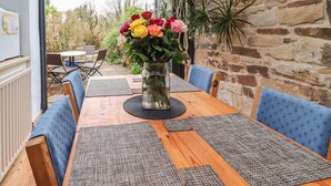 A wooden dining table with blue upholstered chairs, a vase of flowers, and a stone wall in the background. - Ribble Valley Cottage (Preston)