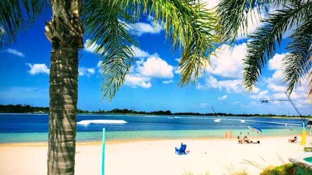 A beach scene with clear blue water, a sandy shore, and palm trees. - Peaceful and Private New House with Hot Tub/ Fire Pit (Spring Hill)