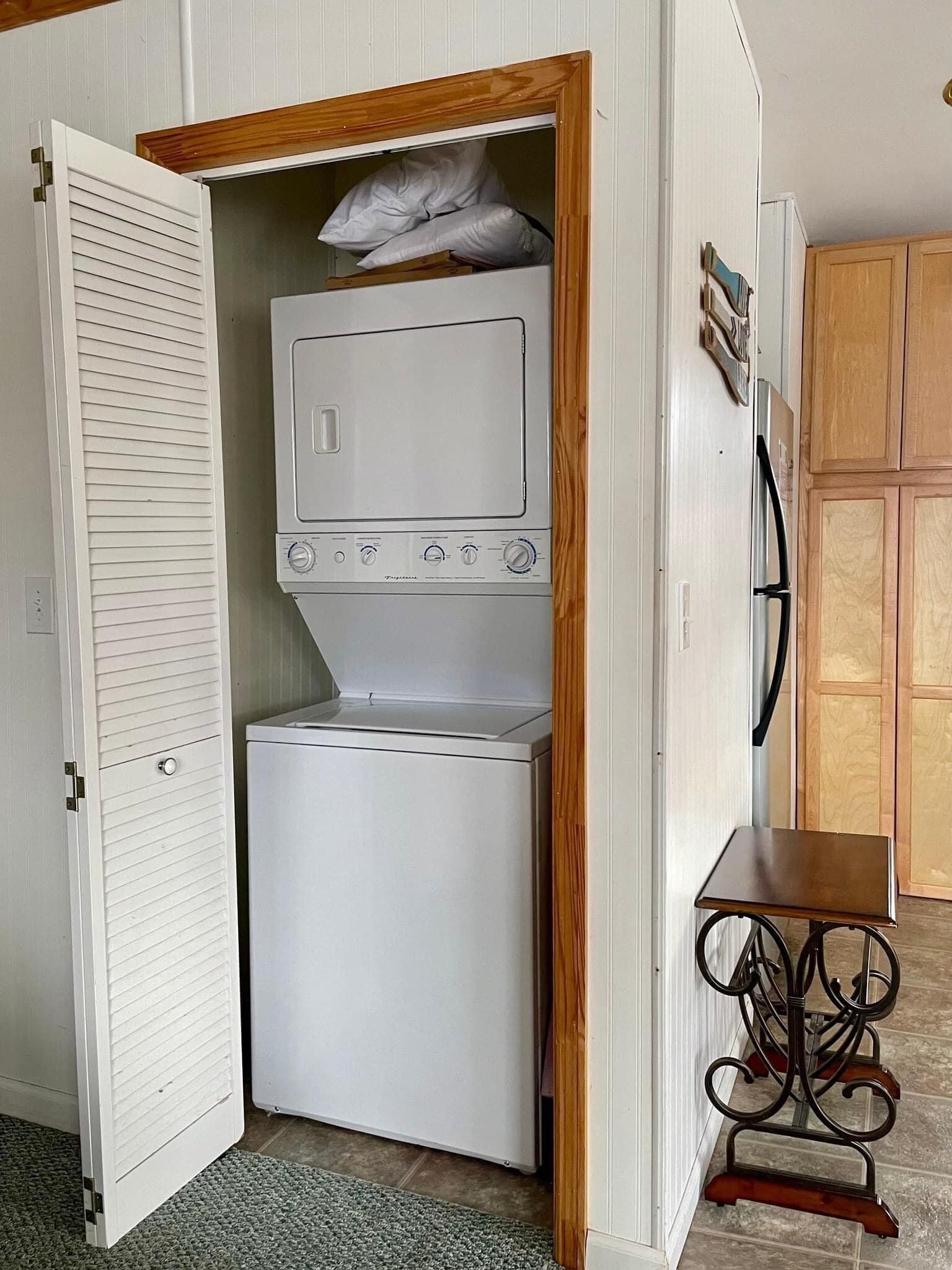 A compact laundry room with a washing machine and dryer, wooden cabinets, and a small table.