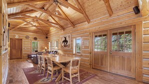 Interior de una cabaña de troncos con comedor, paredes de madera y ventanas amplias.