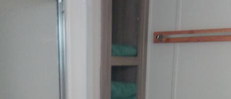 Un baño con inodoro blanco, cabina de ducha y estante empotrado con toallas dobladas.