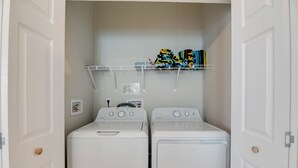 A laundry room with two white washing machines and a metal shelf above them. - New Construction in Venture Out! 3 night minimum stay. (Cudjoe Key)